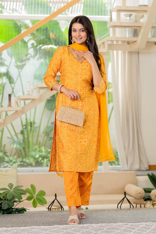 Woman in a bright orange traditional outfit standing indoors with plants in the background