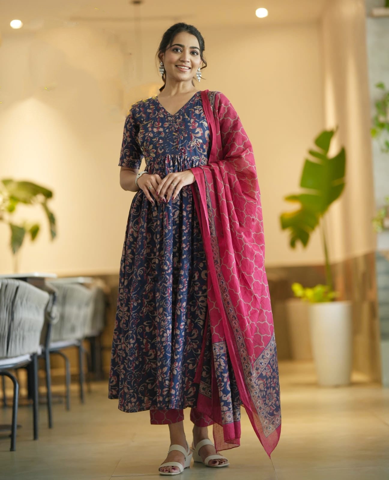 Woman in a floral dress with a pink dupatta standing indoors.