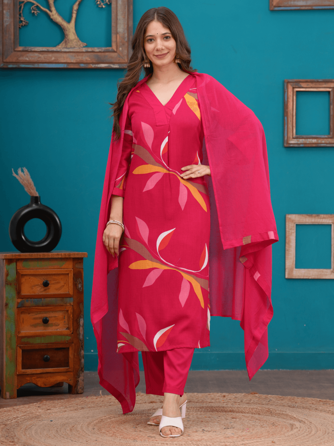 Woman wearing a pink floral dress with a matching dupatta against a teal wall.