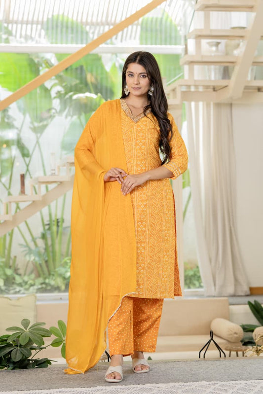 Woman in a yellow traditional outfit standing in a modern indoor setting with plants and a staircase.