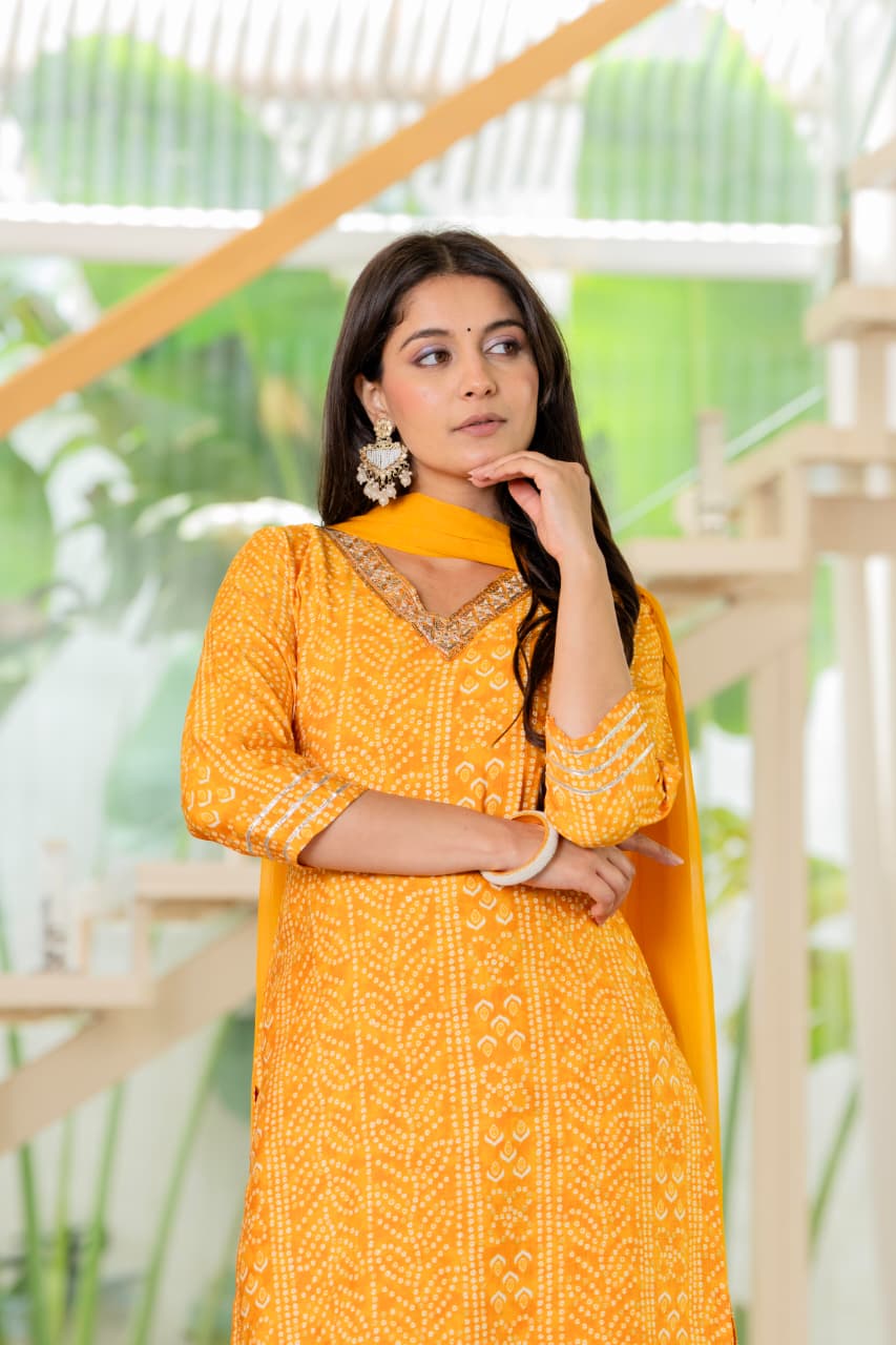 Woman wearing a yellow traditional outfit with intricate patterns, standing outdoors.