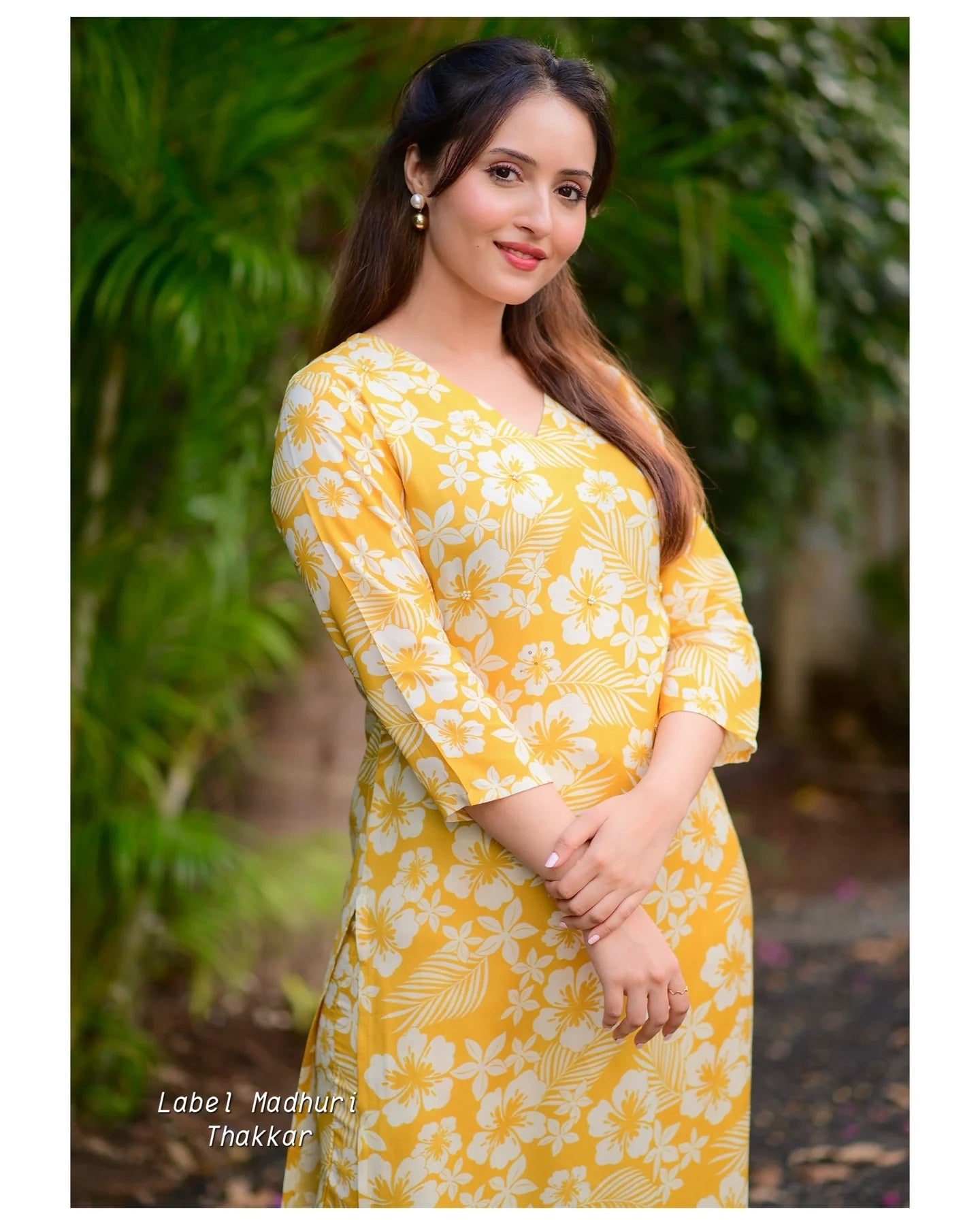 Woman wearing a yellow floral dress with greenery in the background