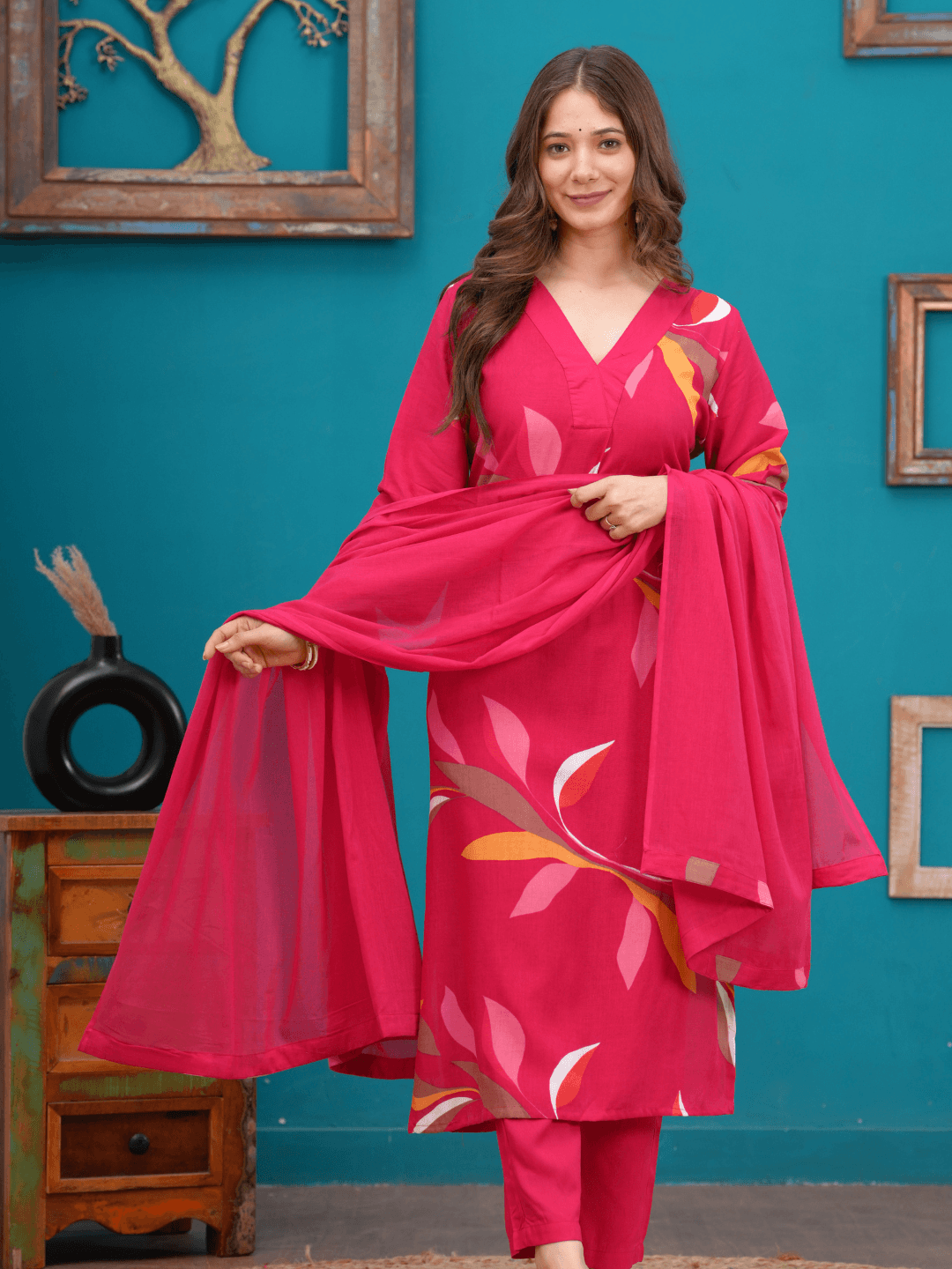 Woman wearing a pink traditional outfit with a matching dupatta against a teal wall.