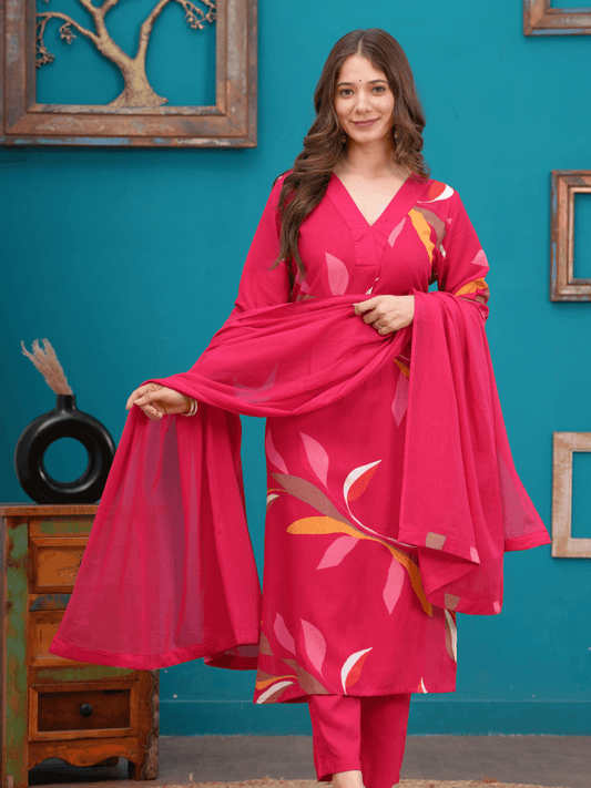 Woman wearing a pink traditional outfit with a matching dupatta against a teal wall.