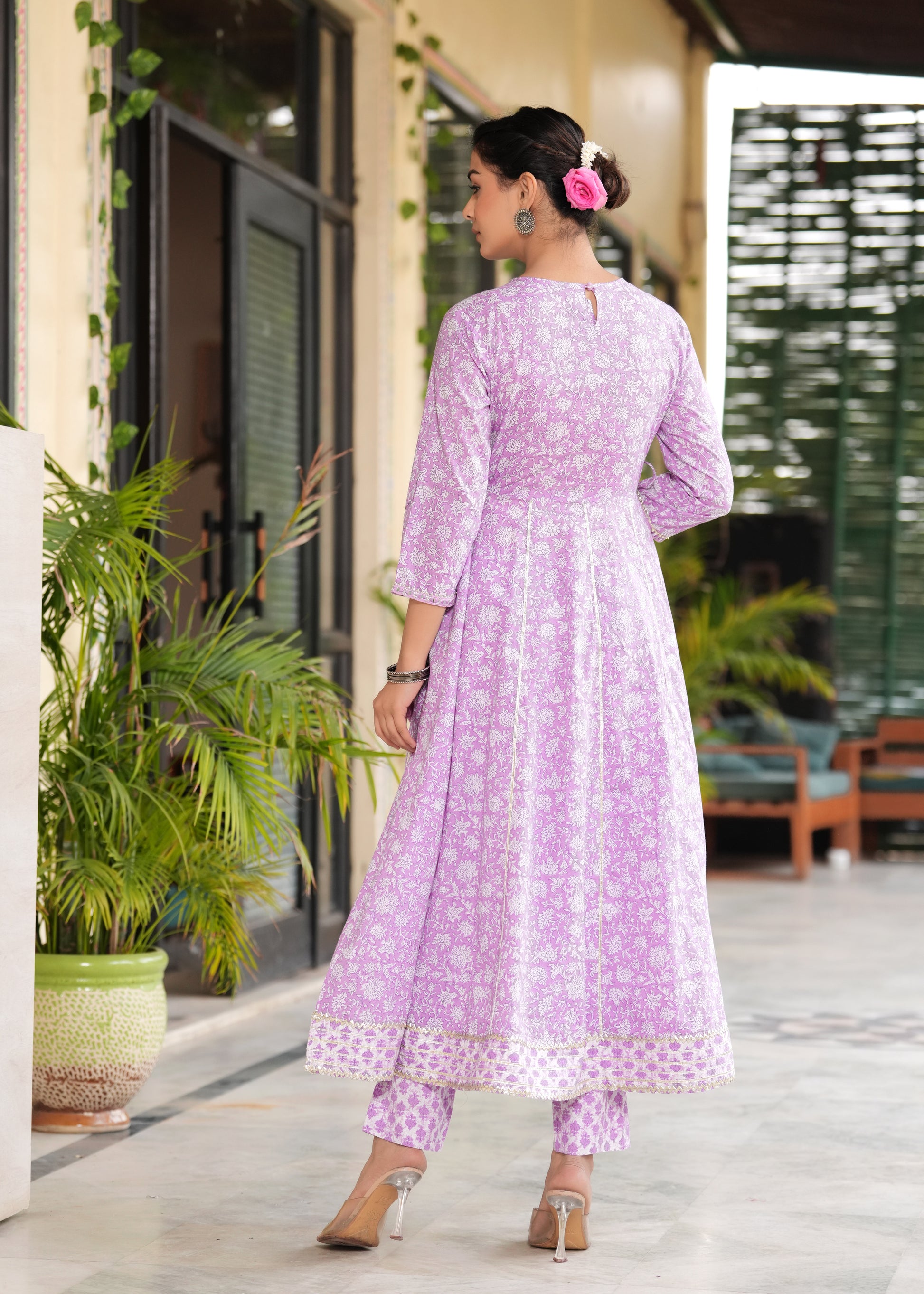 Woman wearing a light purple traditional outfit with white patterns, standing outdoors.