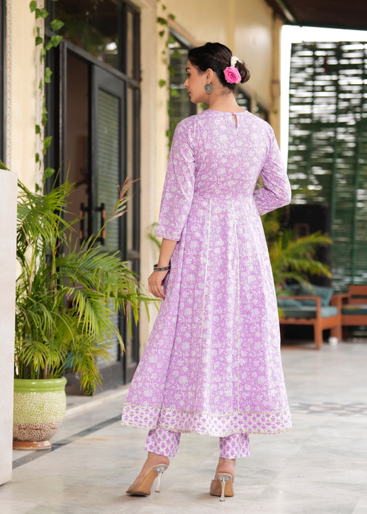 Woman wearing a light purple traditional outfit with white patterns, standing outdoors.
