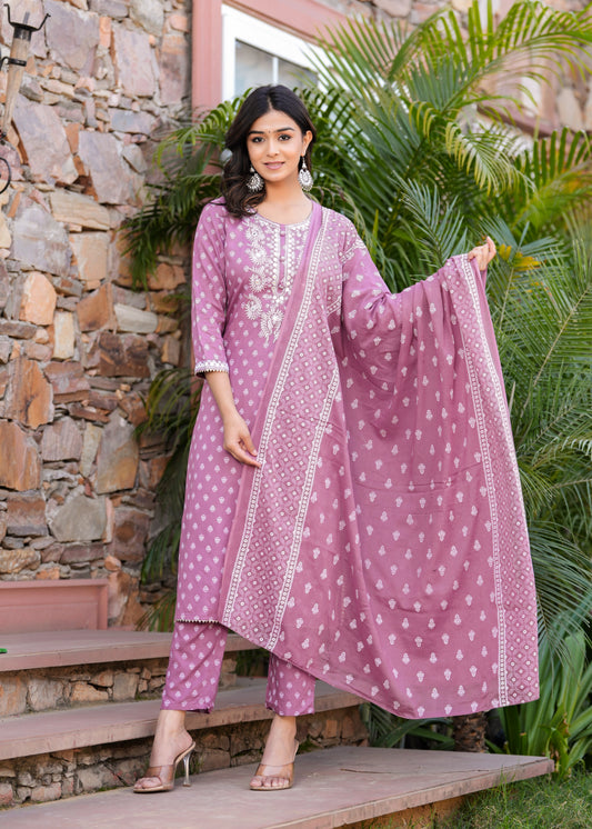 Woman in a pink traditional outfit standing outdoors with a stone wall and greenery in the background