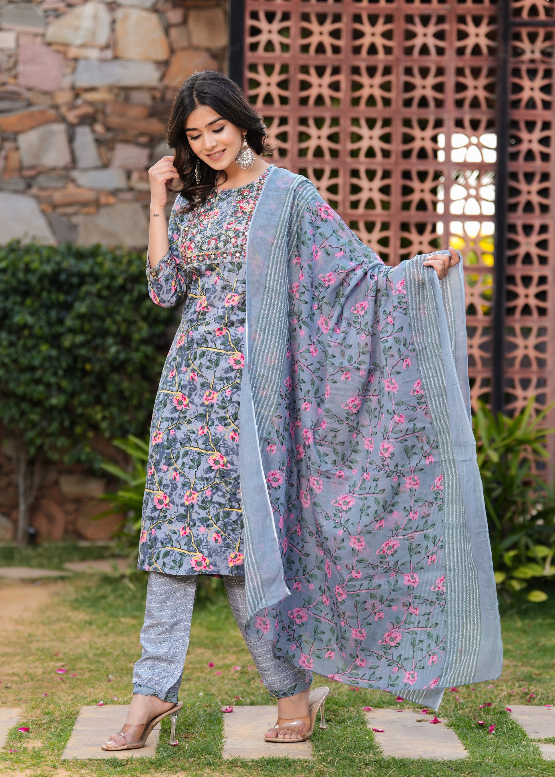 Woman wearing a floral dress with a matching dupatta in an outdoor setting.