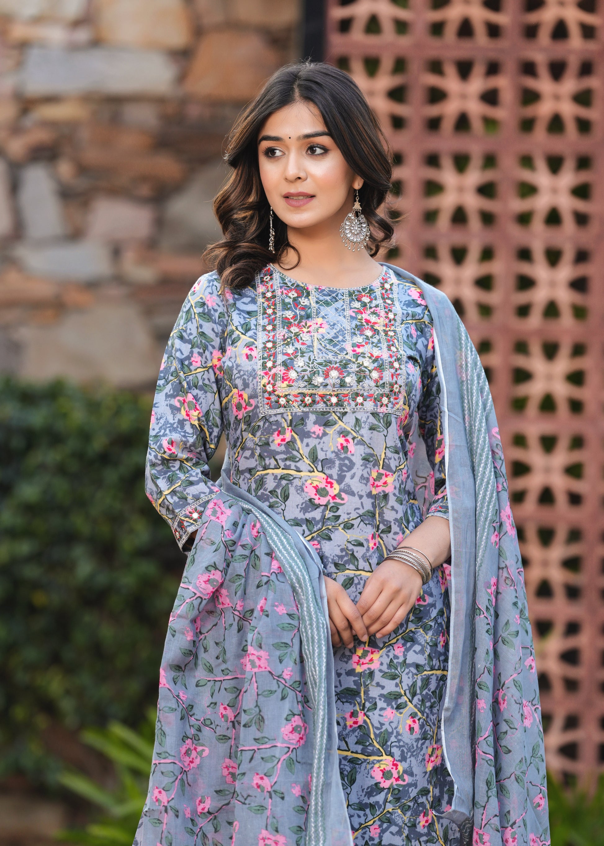 Woman wearing a floral dress with a blue dupatta against a rustic background