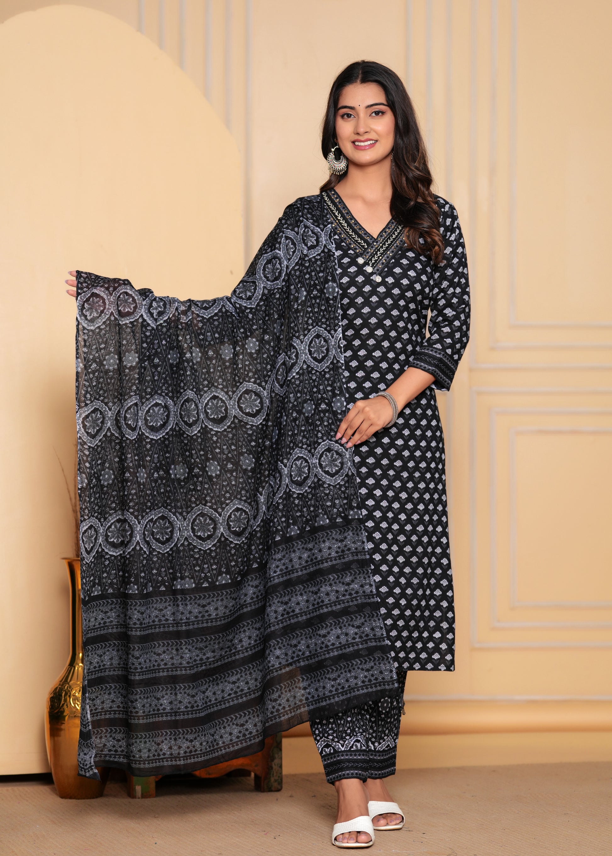 Woman wearing a black and white patterned traditional outfit against a beige wall.