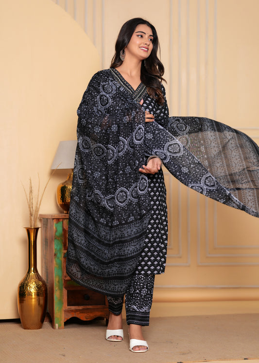 Woman in a black and white patterned traditional outfit with a dupatta, standing indoors against a beige wall.