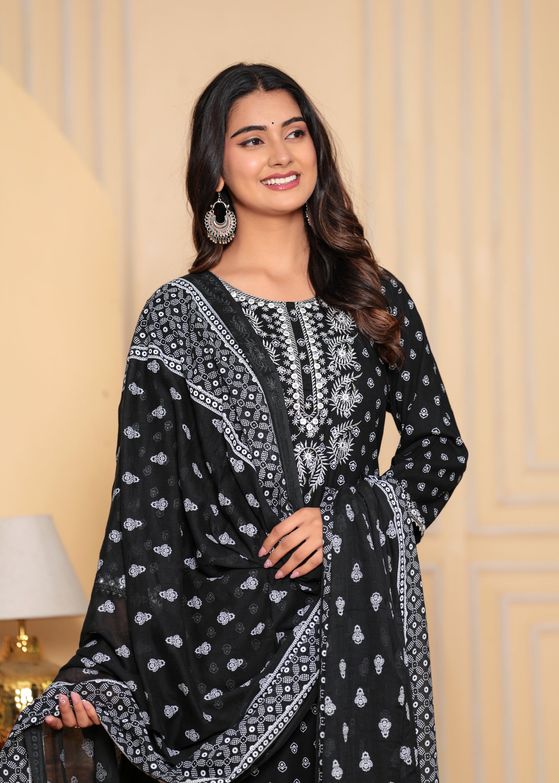 Woman wearing a black and white patterned traditional outfit against a beige wall.