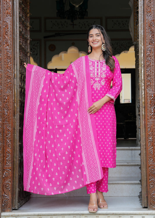 Woman in a bright pink traditional outfit with white patterns standing in an ornate doorway.