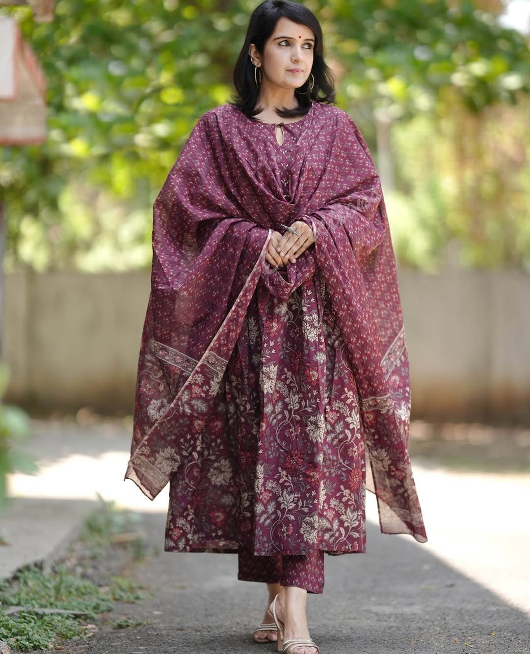 Woman wearing a patterned shawl outdoors with greenery in the background