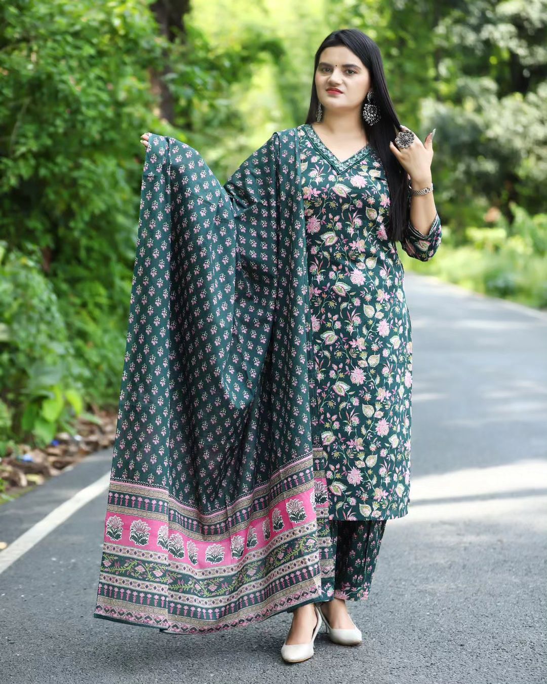 Woman wearing a green floral outfit with a dupatta on a road surrounded by greenery
