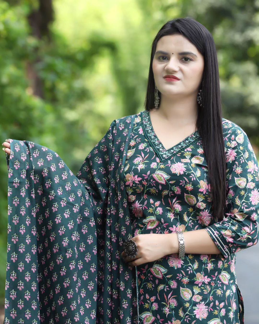 Woman wearing a green floral dress holding a matching dupatta outdoors.