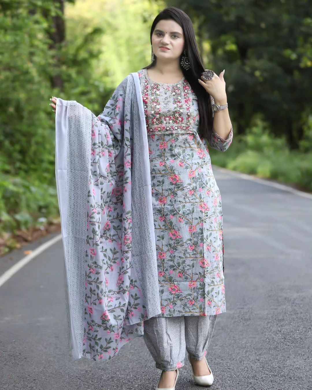 Woman in a floral dress with a dupatta standing on a road with greenery in the background