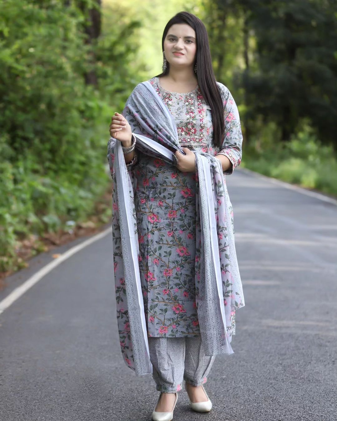 Woman in a floral dress with a dupatta standing on a road with greenery in the background