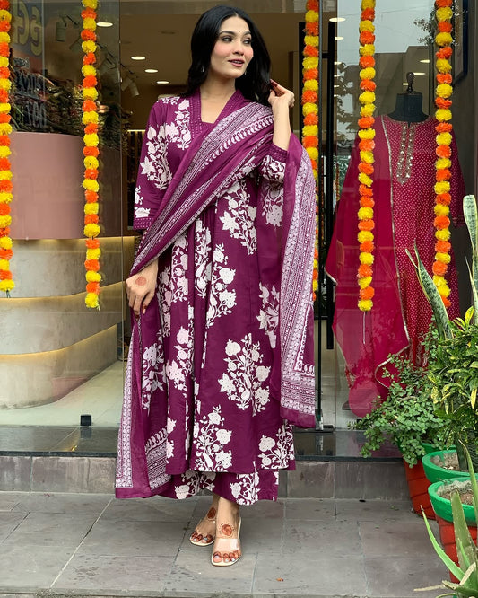 Woman in a purple floral outfit standing in front of a store entrance with decorative elements.