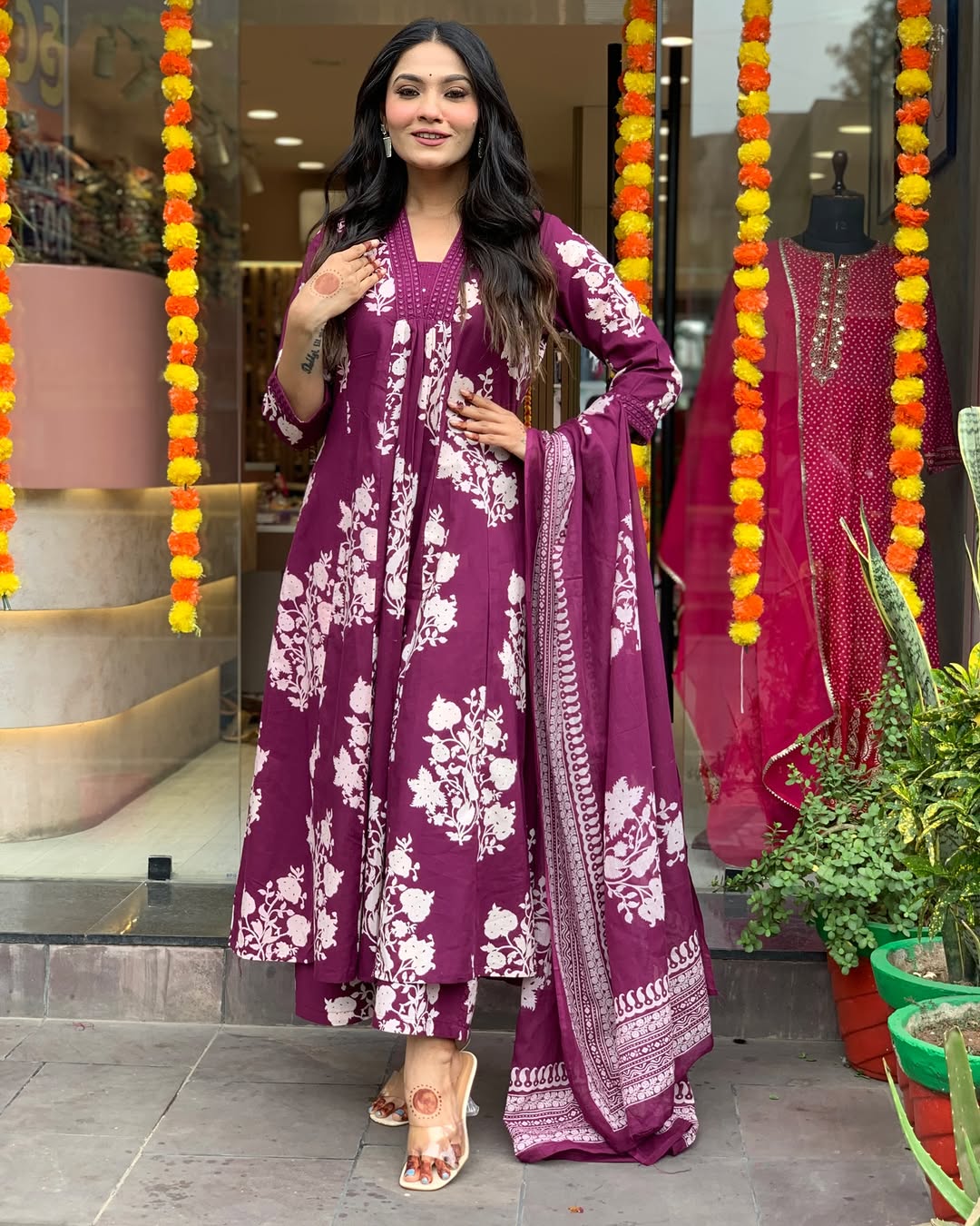 Woman in a purple floral outfit standing in front of decorative items