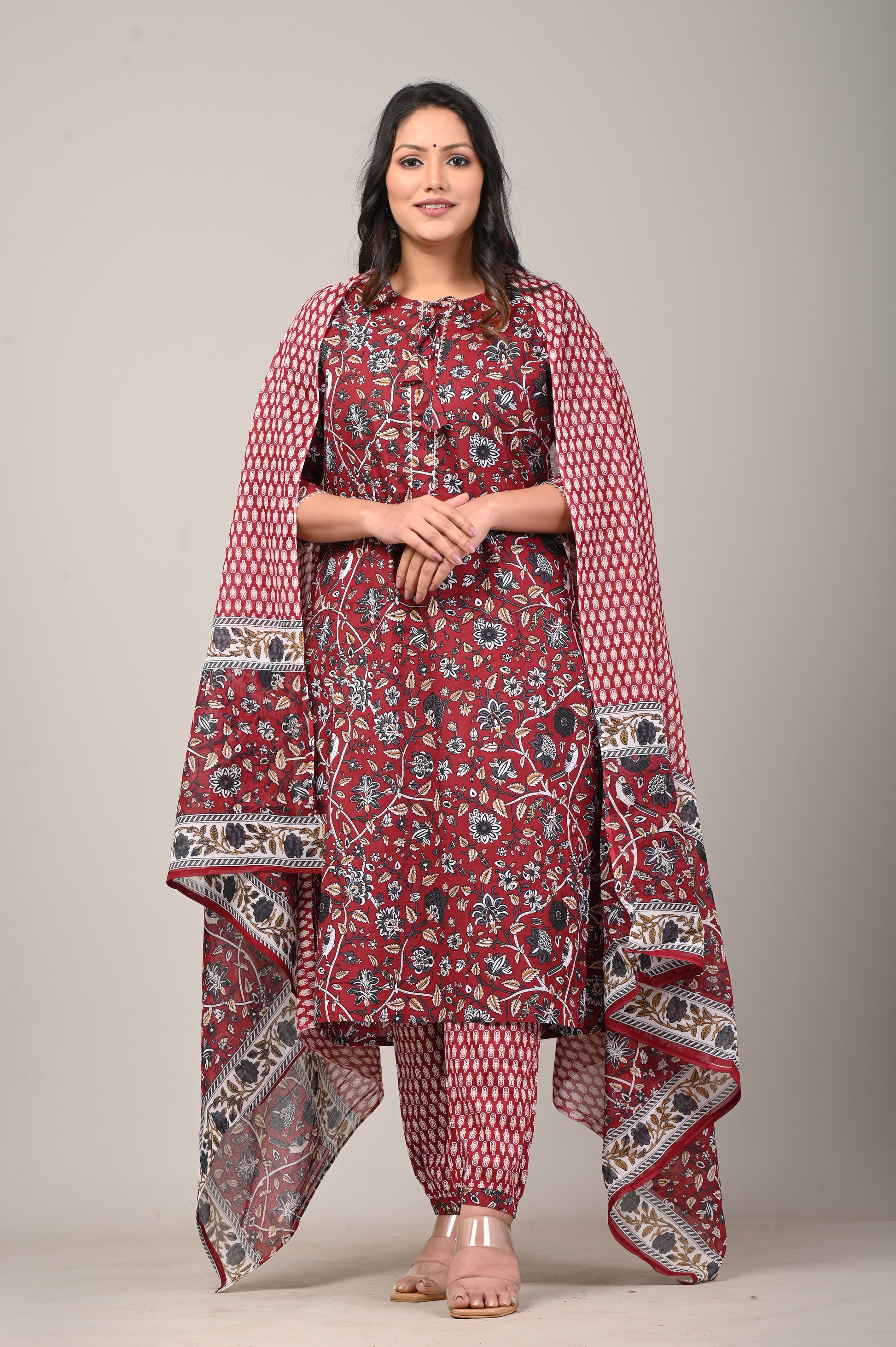Woman wearing a red patterned traditional outfit with a shawl on a plain background