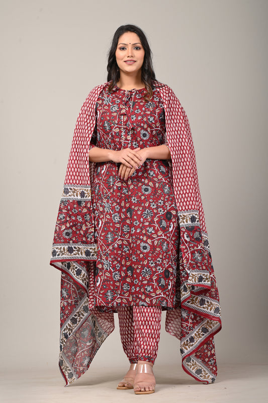 Woman wearing a red patterned traditional outfit with a shawl on a plain background